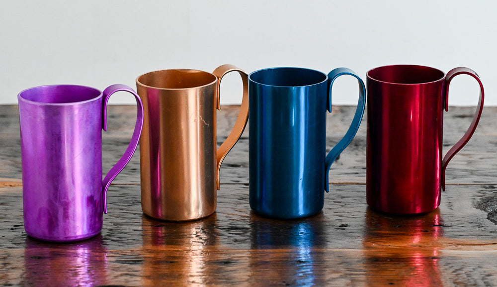 colored metal mugs on wooden table