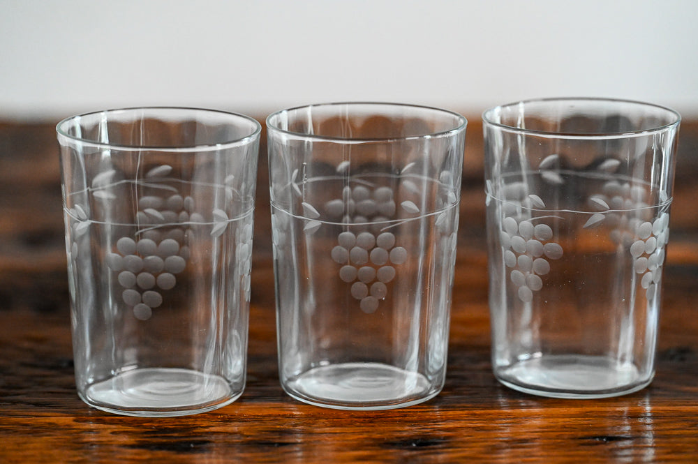 clear juice glasses etched with grapes on wood table
