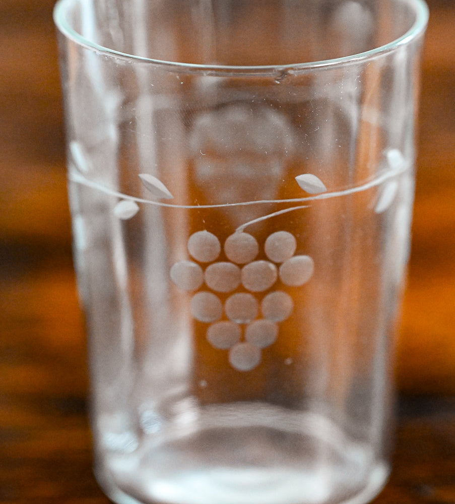 clear juice glass etched with grapes on wood table