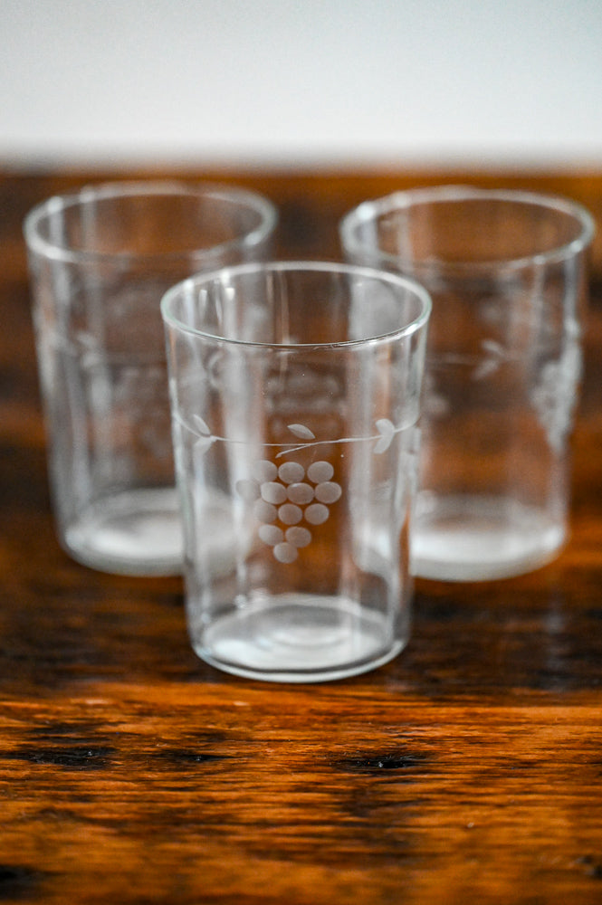 clear juice glasses etched with grapes on wood table
