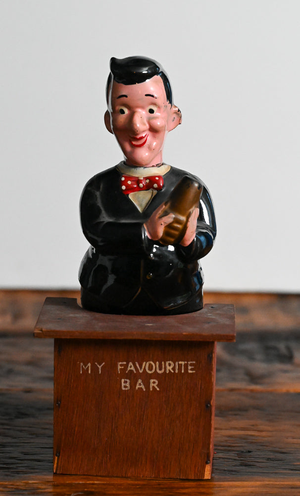 bartender holding a shaker behind a wooden bar decanter, head is the stopper