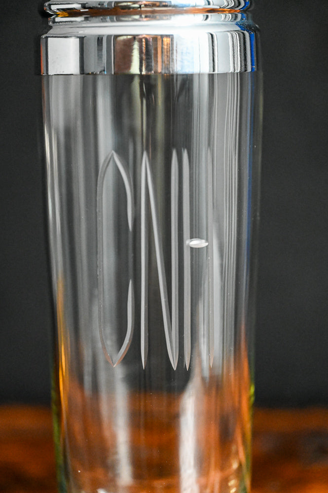 Clear glass cocktail shaker monogrammed with "CNH", metal lid