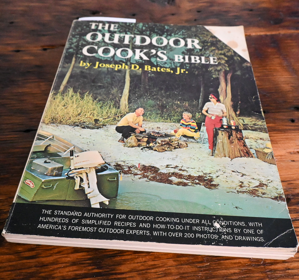 Front cover of Outdoor Cook's Bible with people camping
